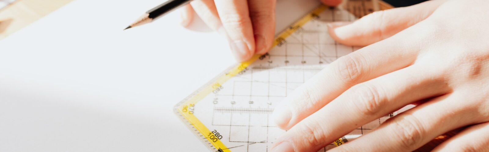 A close-up of a pair of hands using a pencil and set square to measure a drawing.