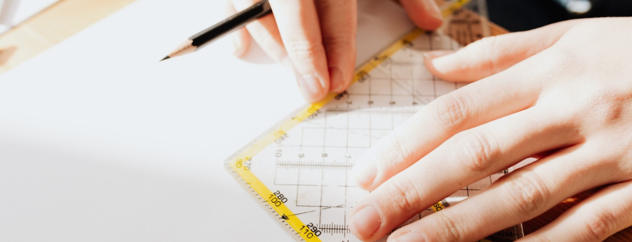 A close-up of a pair of hands using a pencil and set square to measure a drawing.