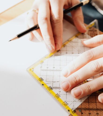 A close-up of a pair of hands using a pencil and set square to measure a drawing.