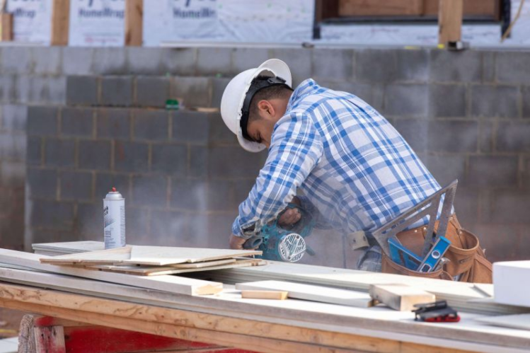A construction worker cuts a fiber cement siding board on a job site.