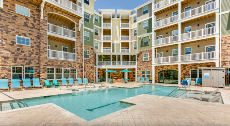 A multi-level commercial apartment building with fiber cement siding overlooks a modern swimming pool.