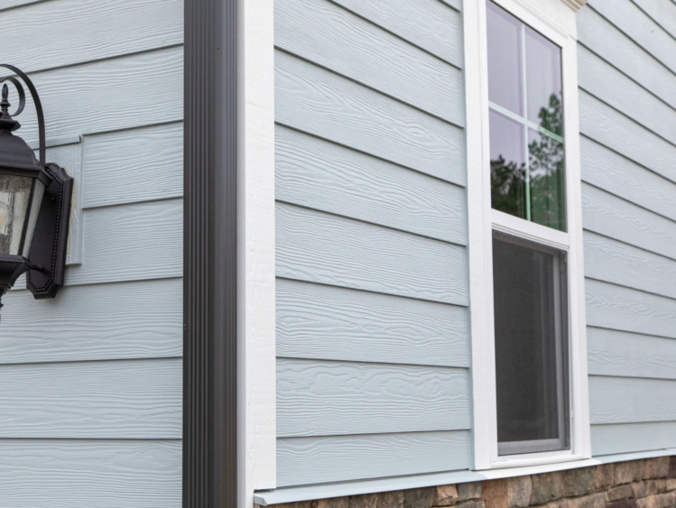 Pale blue siding on the side of a home with white-trim windows.
