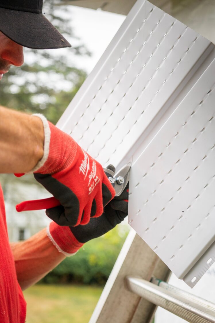 A close-up of a man in red and black gloves cutting white trim.