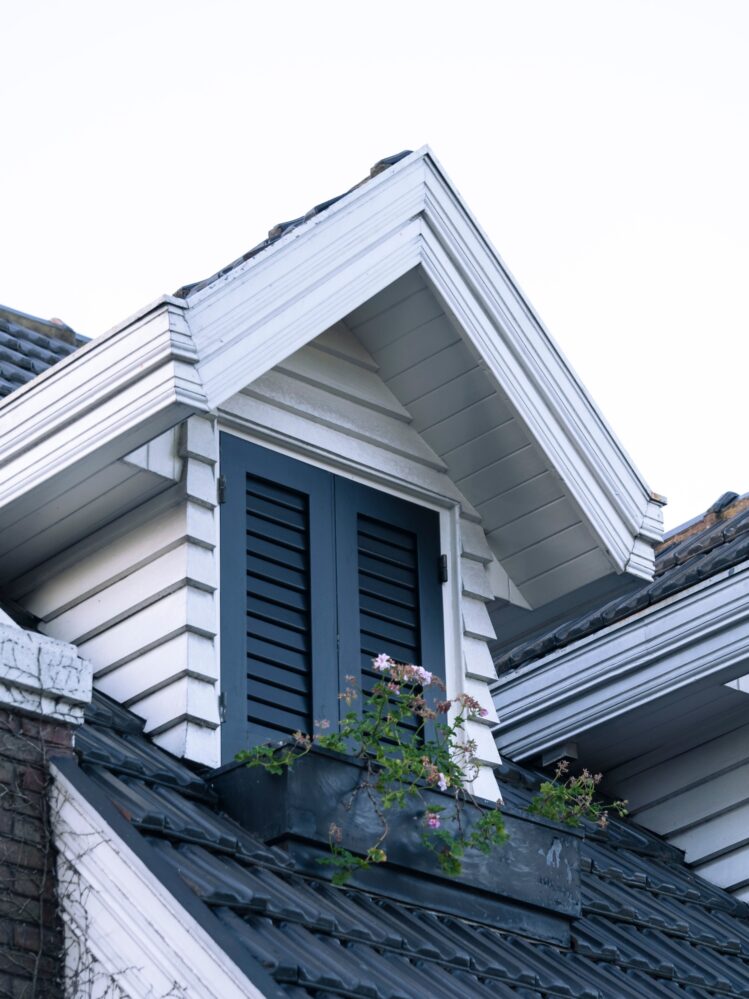 Gable roof with a dormer window featuring shutters and a flower box against a clear sky.