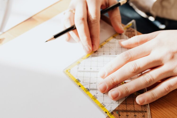 A close-up of a pair of hands using a pencil and set square to measure a drawing.