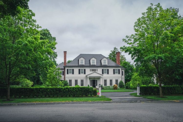 A white house with black shutter and beautiful greenery and trees